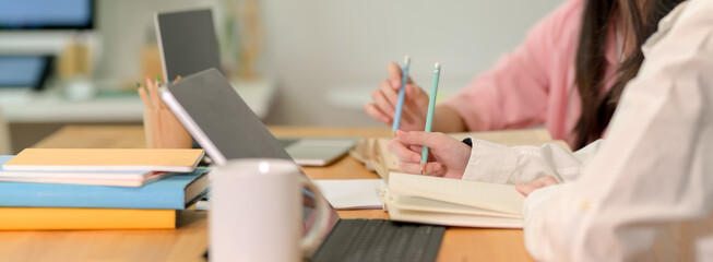 Female college students preparing their upcoming exam together with digital tablet, book and...