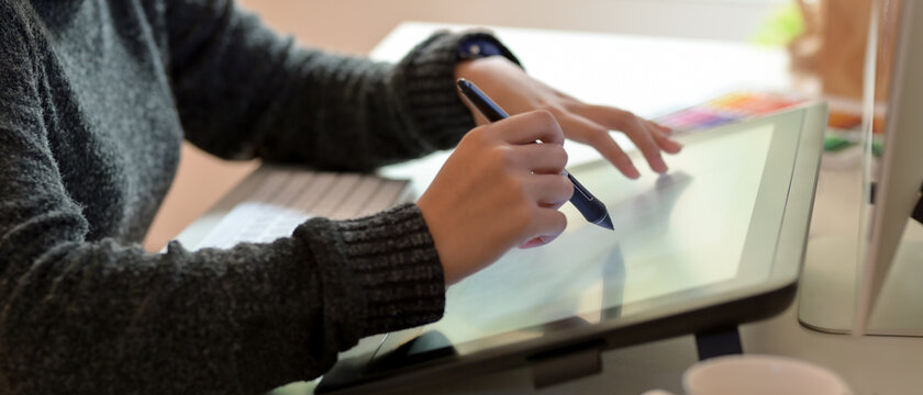 Female graphic designer working on drawing tablet with stylus pen in office room
