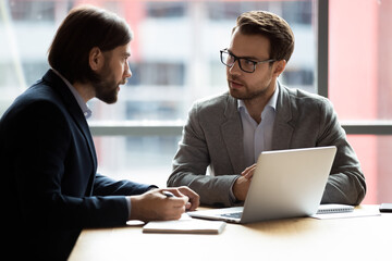 Mentoring, brainstorming, partnership, communication during business meeting concept. Two confident caucasian entrepreneurs businessmen in formal suits sitting at desk talking solving common issues