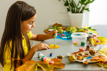Obraz na płótnie Canvas Little girl painting on autumn yellow leaves with gouache, kids arts, children creativity, autumn art.