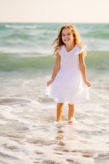 Fototapeta na wymiar girl in white dress walks and fun on sea shore with big waves and strong winds.