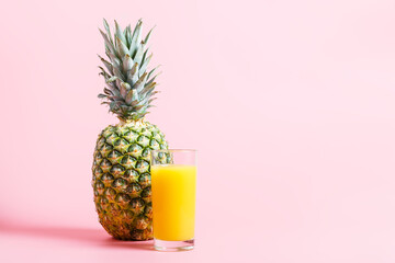 Fresh ripe pineapple and a glass of pineapple juice on a pink background. hot summer concept. copy space, minimalism.