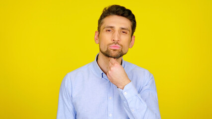 Brutal bearded man straightens his beard with his hand. Handsome guy in a light blue shirt on a yellow background with copyspace. Place for text or product