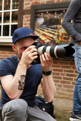 Junger Fotograf mit blauer Kappe hält eine große Kamera DSLR in der Hand mit einem Teleobjektiv,...