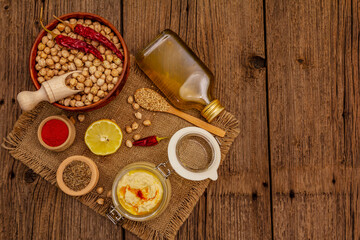 Obraz na płótnie Canvas Hummus on old wooden boards background. Dry chickpea, olive oil, lemon, cumin and chili pepper