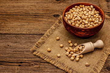 Obraz na płótnie Canvas Dry chickpea in ceramic bowl on old wooden boards background. Traditional ingredient for cooking hummus