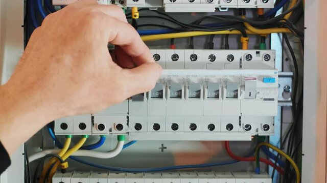 Close-up Of Hand On Switch Of Distribution Board. Man switching on fuseboard