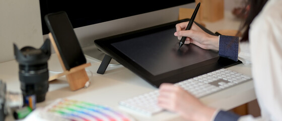 Graphic designer working on drawing tablet with stylus pen, computer and supplies on white office...