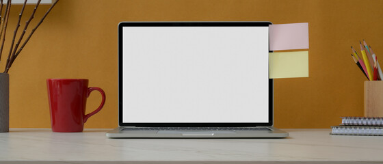 Home office desk with mock-up laptop, stationery, mug and sticky note on white table