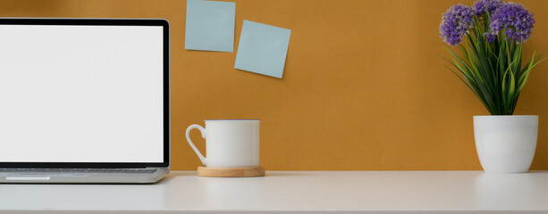 Comfortable workspace with mock-up laptop, cup, flower pot and copy space on white table