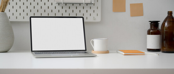 Minimal worktable with blank screen laptop, cup, schedule book and decorations on white table