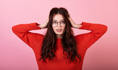 Obraz na płótnie Canvas Beautiful young long-haired lady in a sweater and glasses on a pink background.
