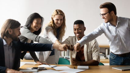 Horizontal image middle-aged and young five multiracial staff members gather in boardroom show unity stacked hands in circle, fists bumping symbol of togetherness common goals business loyalty concept