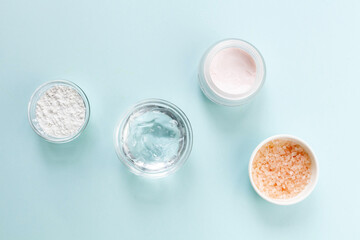 Skin care cosmetics: gel, face cream, alginate mask, sea salt on blue background, top view