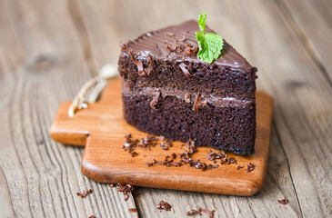 Cake chocolate delicious dessert served on the table - cake slice on wooden cutting board background with chocolate and mint leaf
