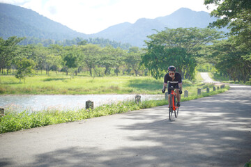 Fototapeta premium Male athletic ride bicycle in a view of green forest and mountain. Vacation activity outside in summer after pandemic, people want to have a sport outdoor in nature like mtb or trail speed biking. 
