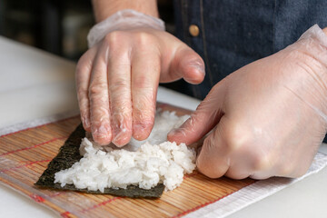 Sushi chef wearing gloves lays the rice on the nori