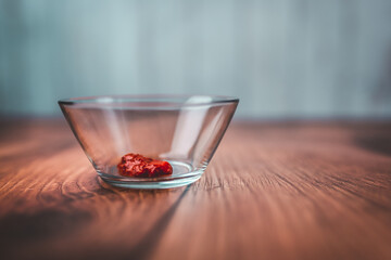 A measure of 1 TBSP of Chilli paste in a transparent glass bowl on a brown wooden table with bright wooden background. Free space for your decoration/text.