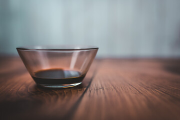 A measure of 1 TBSP of Soya Sauce in a transparent glass bowl on a brown wooden table with bright wooden background. Free space for your decoration/text.