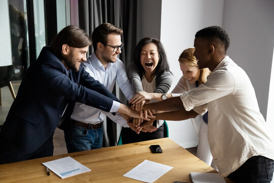 Team building activity concept. Cheerful 5 diverse workmates stack palms arms together celebrate share common success, succeed business goal together give high five symbol of loyalty and companionship