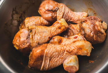 Close-up of a bowl full of marinated FRESH RAW ORGANIC CHICKEN DRUMSTICK with lots of spices on a dark brown wooden table.