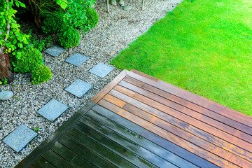 partially cleaned wooden terrace with a pressure washer by the green lawn in the garden