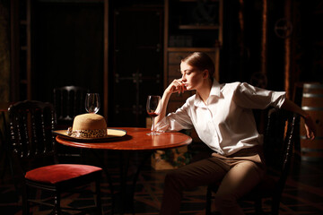 Beautiful theatrical actress woman with retro fashion style on the stage siting near wooden table...