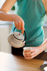 Close up woman hands pouring tea while waiting her friends in a sunny living room