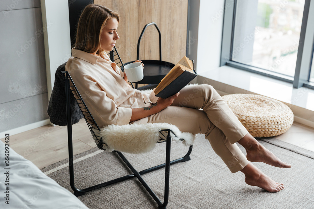 Sticker Image of woman drinking tea and reading book while sitting on armchair