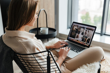 Image of focused woman working with laptop while sitting on armchair