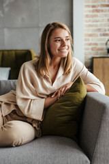 Image of woman smiling and looking aside while sitting on sofa