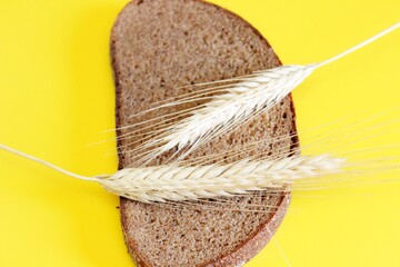 A piece of rye claid and rye ear laid on a yellow background