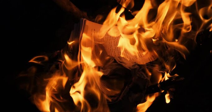 Education book on fire. Big bright flame, burning paper on old historic cultural publication. Destruction English diary journal with Latin characters. Bonfire conflagration in slow motion in the dark