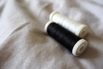 Fototapeta na wymiar two plastic skeins of black and white silk threads on a gray cotton fabric . hobby sewing