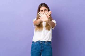Young woman over isolated purple background making stop gesture with her hand to stop an act