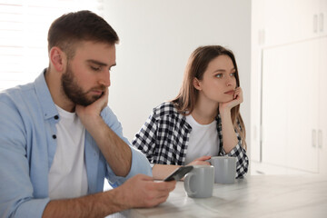 Young man preferring smartphone over his girlfriend at home. Relationship problems