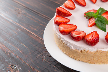 Delicious cheesecake with fresh strawberries and mint, homemade recipe without baking, on a wooden table. Copy space.