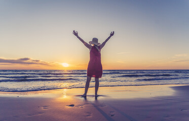 Fototapeta na wymiar Woman in red with arms outstretched by the sea at sunrise enjoying freedom and outdoors life