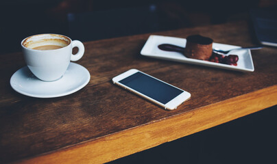 Close up of mobile phone lying on a wooden table near cup of cappuccino 