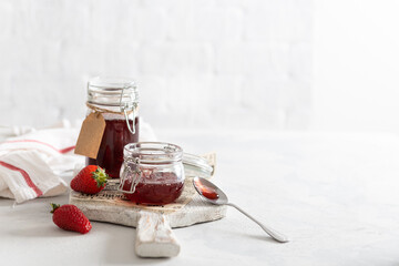 Homemade strawberry jam or marmalade in the glass jars and ripe strawberries on the wooden board on white background. Side view, copy space for text or product. Cookbook recipe. Preserve food