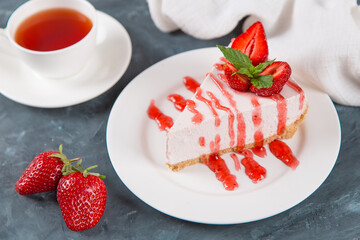 Sweet breakfast, tea and delicious cheesecake with fresh strawberries and mint, homemade recipe without baking, on dark blue stone table. Copy space.