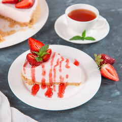 Sweet breakfast, tea and delicious cheesecake with fresh strawberries and mint, homemade recipe without baking, on dark blue stone table. Copy space.