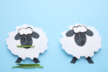 Paper sheeps on light blue background, flat lay. Concept of jealousy