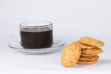 Closeup of the cereal cookies is stacked in multiple pieces and the cookies are brown and a cup of coffee is placed behind them. The image has blank space beside the object and has a white background.