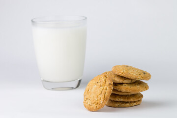Closeup of the cereal cookies is stacked in multiple pieces and the cookies are brown and a cup of milk is placed behind them. The image has blank space beside the object and has a white background.