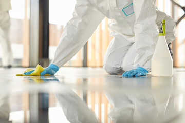 Close up of unrecognizable worker wearing protective suit cleaning floor with chemicals during disinfection indoors, copy space - obrazy, fototapety, plakaty