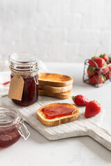 Sweet homemade strawberry jam with toasts and fresh berries on white wooden board on rustic white background. Side view, close up. Cookbook recipe. Social media content. Summer strawberry confiture