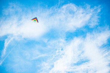 Beautiful kite in bright colors of the rainbow flies against a sunny blue sky. Concept childhood of freedom and naivety. Advertising space