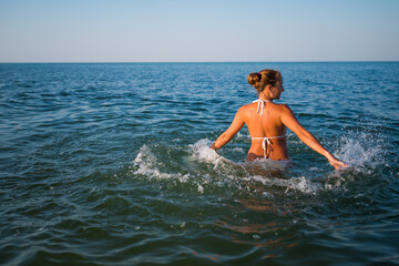 Rear view of a pretty young woman swimming in the sea on a sunny warm summer day. The concept of rest and enjoyment of tourist trips. Copyspace