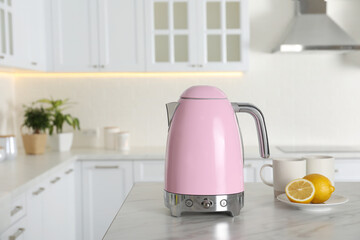 Modern electric kettle, cups and lemons on table in kitchen